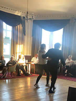 Two women dancing in hotel with visitors watching