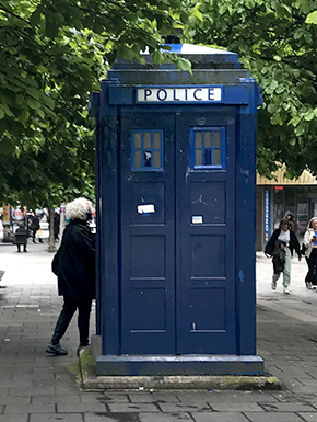 Blue police box on pedestrian mall, closer still, with me walking behind