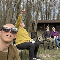 All of us in chairs by the cabin: Ben wearing sun glasses and eclipse glasses